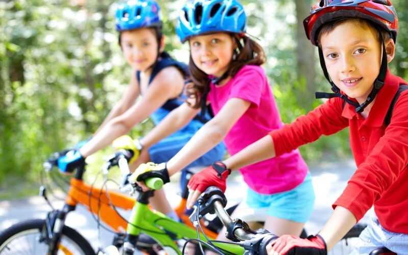 drie kinderen in kleurrijke kleding op de fiets met fietshelmen op