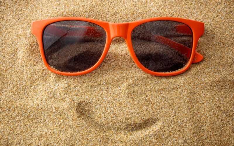 rode zonnebril in het zand met een smiley lach eronder