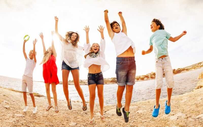 vijf tieners springen in de lucht op het strand